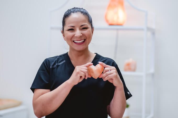 A therapist smling towards the camera while holding a heart stone