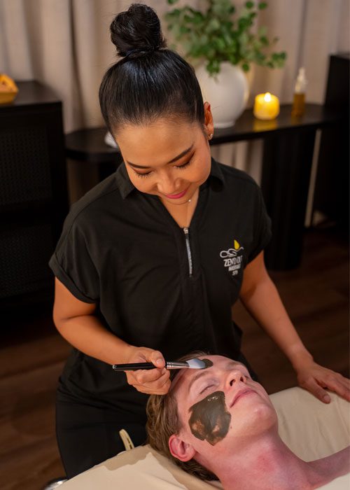 GC-faq A therapist applying a facial mud mask to a relaxed client.