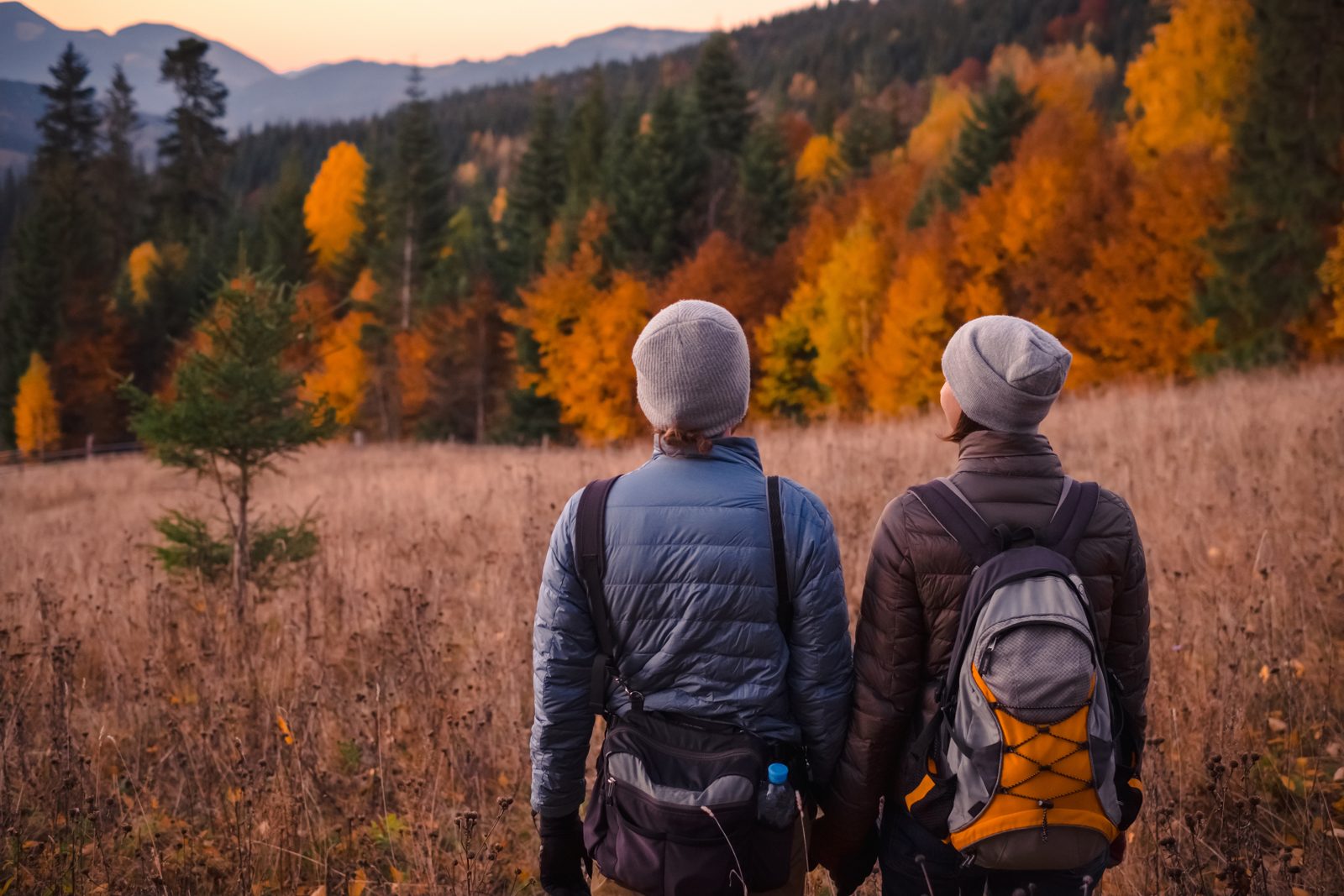 Couple in hats and jackets looking out over an autumn mountain landscape