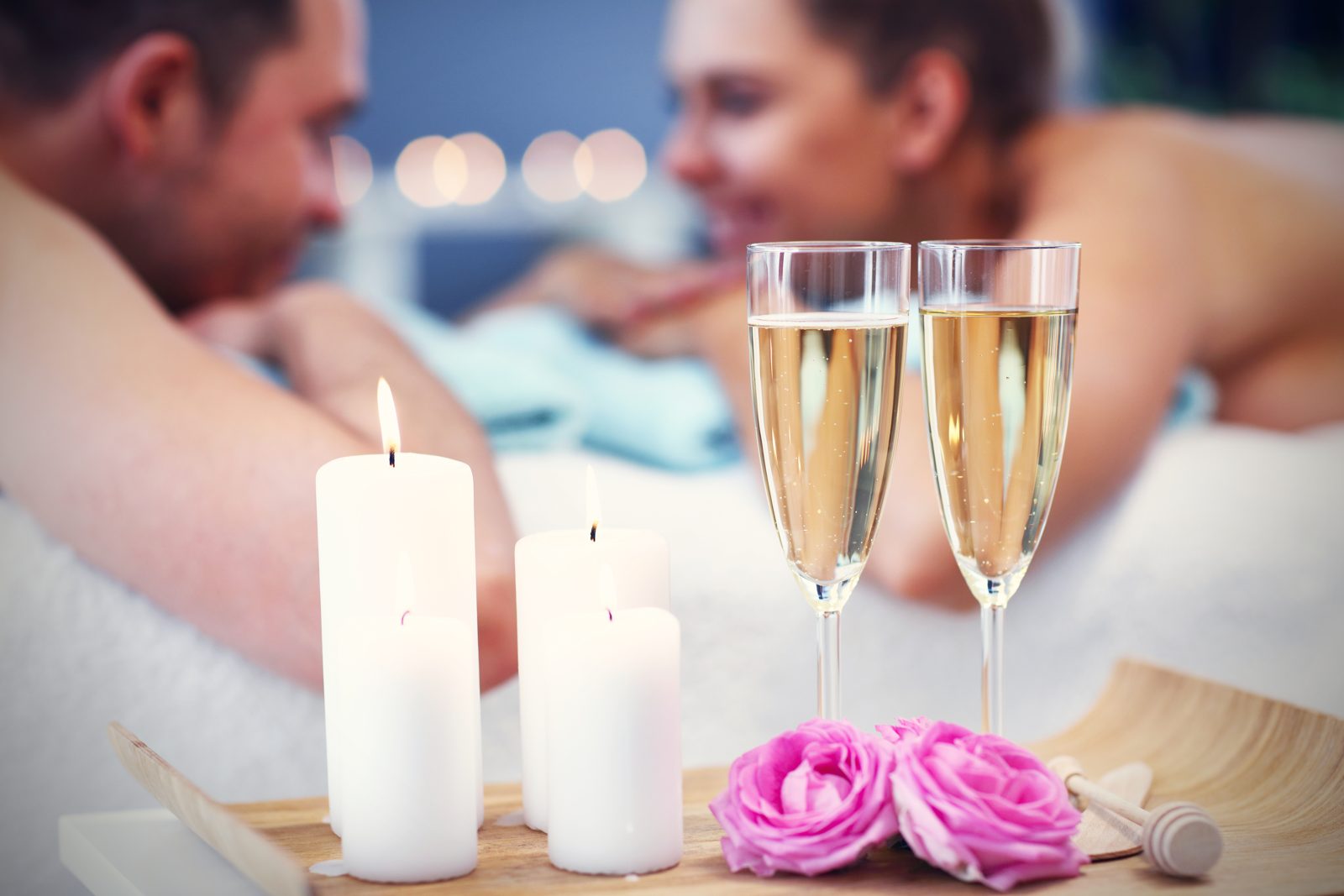 Candles and two glasses of sparkling wine beside a couple relaxing on massage tables